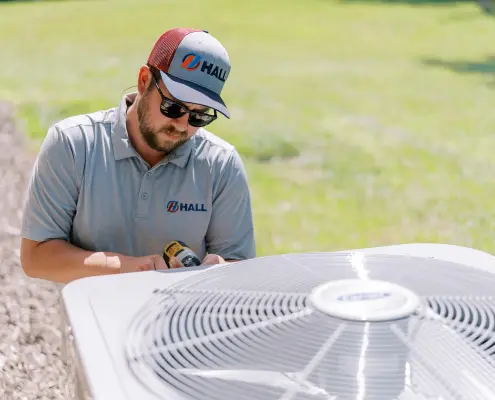 Hall technician servicing an HVAC unit outside home.