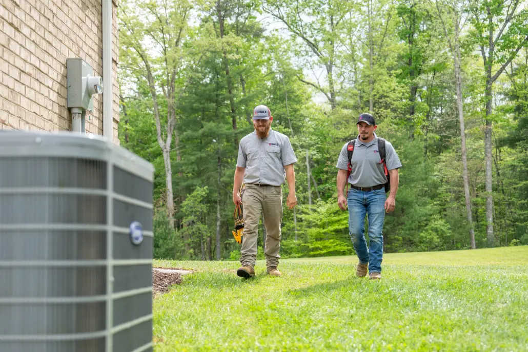 HVAC technicians walking up to an outdoor unit with tools