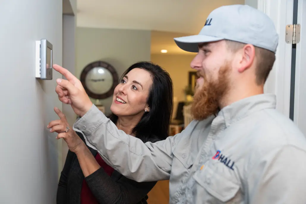 HVAC tech adjusting the thermostat with the homeowner