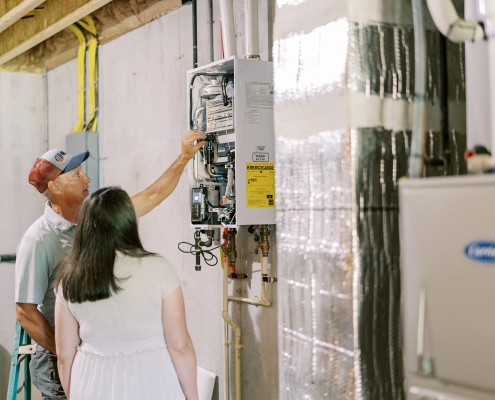 technician showing inside of tankless water heater to customer in basement.