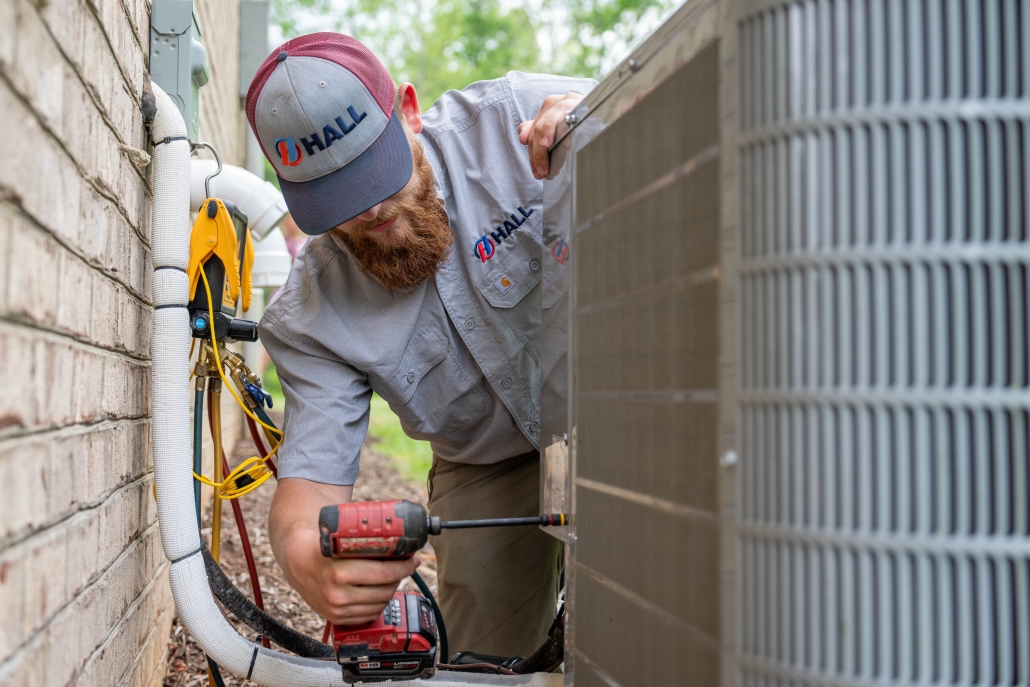 HVAC technician working on an outdoor unit with a drill